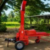 Red forage chopper with a tall vertical discharge chute mounted on a trailer, outdoors in a rural yard.