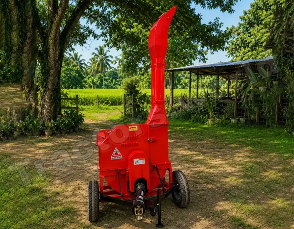 Red portable wood chipper on wheels in a rural yard with green fields and trees behind it.