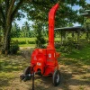 Red portable wood chipper on a trailer, outdoors among trees with a tall curved chute ready to shred branches.