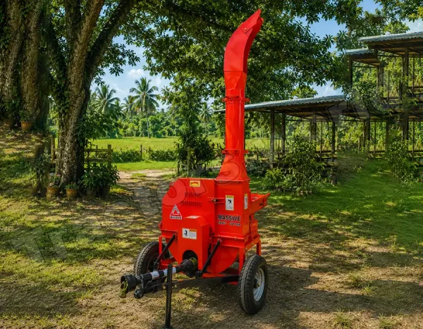 Red portable wood chipper on a trailer, outdoors among trees with a tall curved chute ready to shred branches.