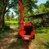 Red wood chipper on a trailer in a sunny yard with palm trees and a wooden shed nearby.